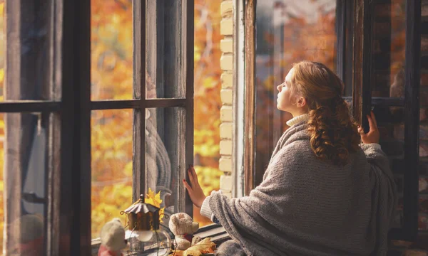 Happy young woman enjoying fresh autumn air at open window