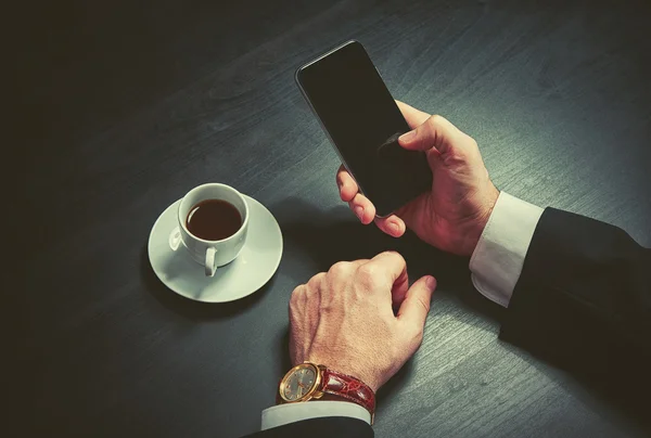 Phone and a cup of coffee in the hands of a businessman in dark colors