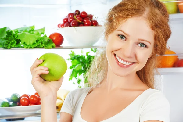 Happy woman with apple and open refrigerator with fruits, vegeta