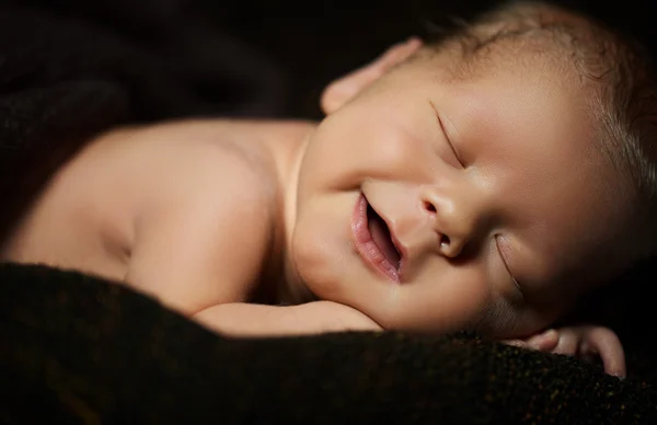 Happy newborn baby smiling in his sleep on a dark