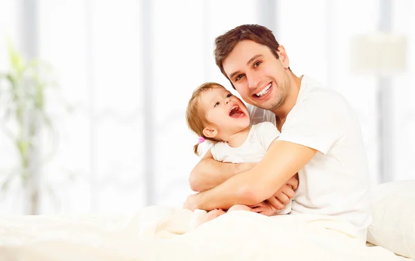 Happy family father and child daughter playing in bed