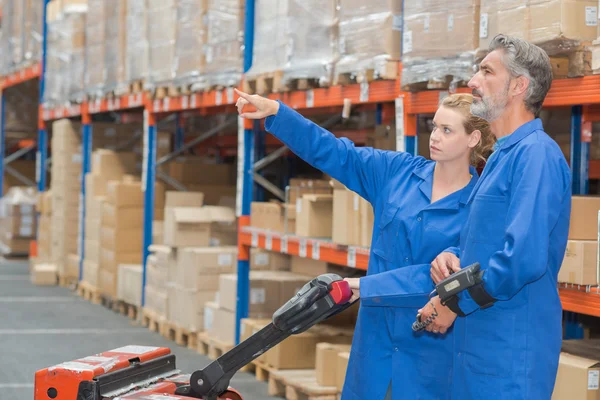 Two warehouse workers with pallet truck, pointing