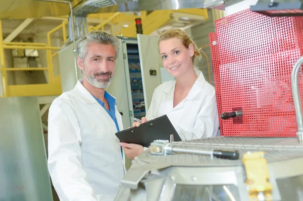 Man and woman with clipboard next to machine