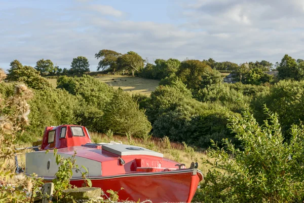 Old boat aground amid green country near Looe, Cornwall