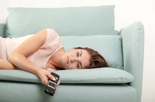 Sleepy young woman lying on couch holding TV remote control. Casual style indoor shoot