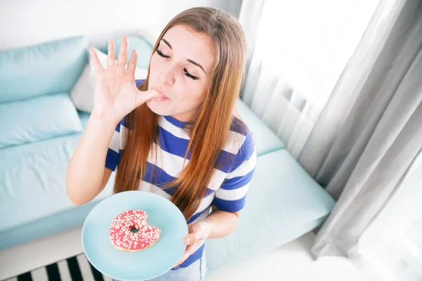 Woman at home eating donut and licking her finger