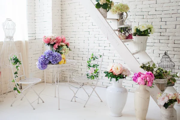 Flowers, openwork metal furniture, a mannequin in the interior of the white room close-up.