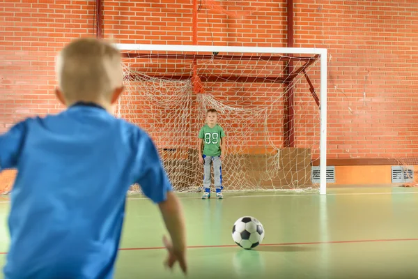 Two young boys playing soccer on an indoor court