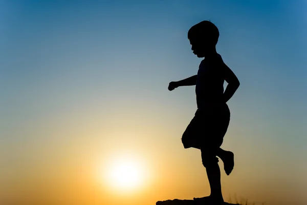 Little boy kicking the setting sun