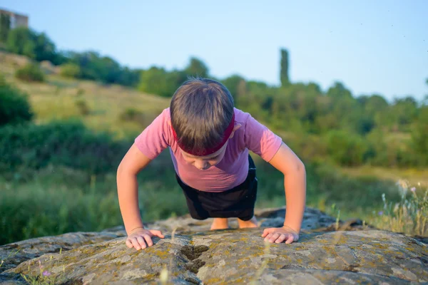 Sporty Young Boy Doing Push up on Top of Boulder