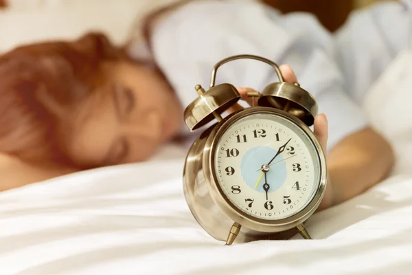 Young Asian woman in bed trying to wake up with alarm clock