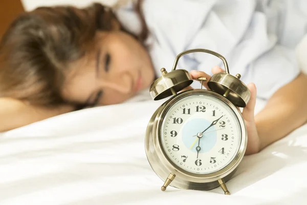 Young Asian woman in bed trying to wake up with alarm clock