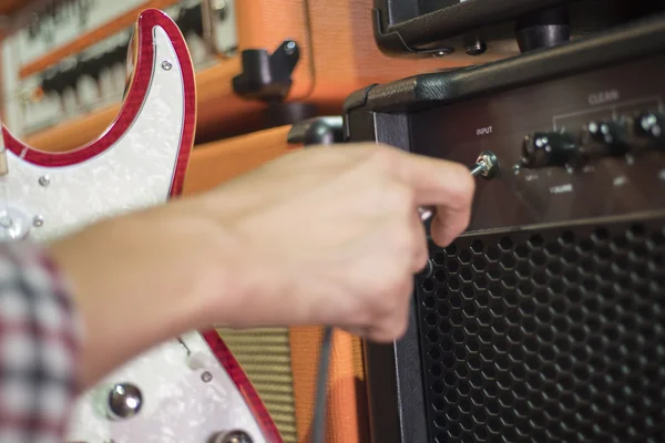 Closed up hand holding jack plug-in to the guitar amplifier