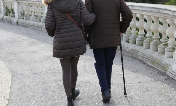 Woman accompanies the older gentleman with walking stick
