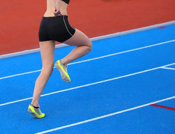 Young woman running on the athletics track with blue colored lan