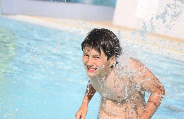 Young boy under the powerful jet of water in the pool in summer