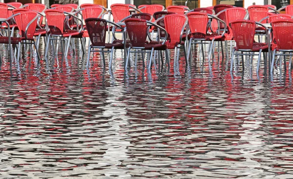 Venice, red chairs with water at high tide