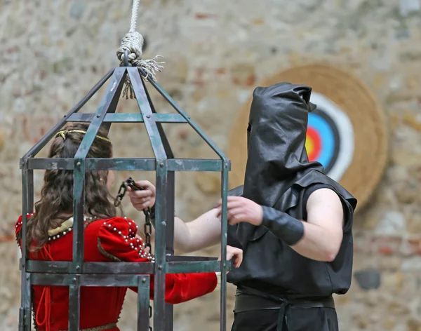 Medieval EXECUTIONER with black cap on head and girl in cage