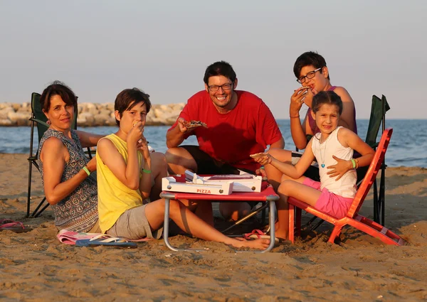 Happy family of five person  eats pizza on the beach