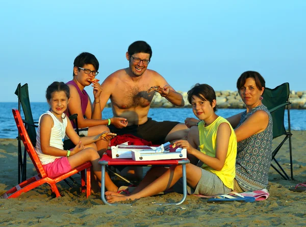 Happy family of five person eats pizza on the beach