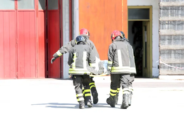 Four firefighters in action carry a stretcher with injured