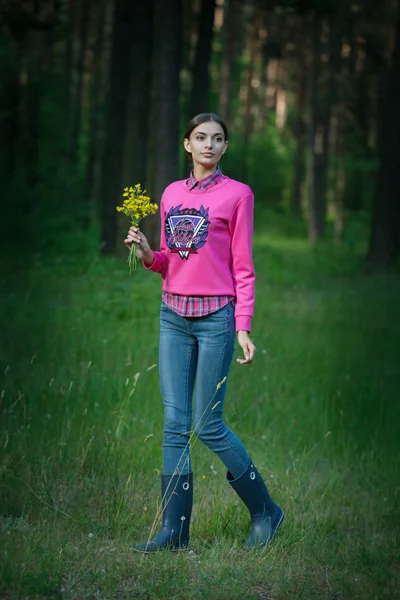 Young beautiful woman walks in the forest with flowers