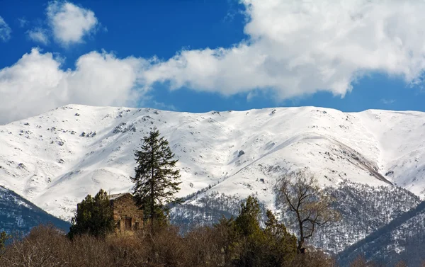 Old house on the hill with trees in the background of snowy mountains