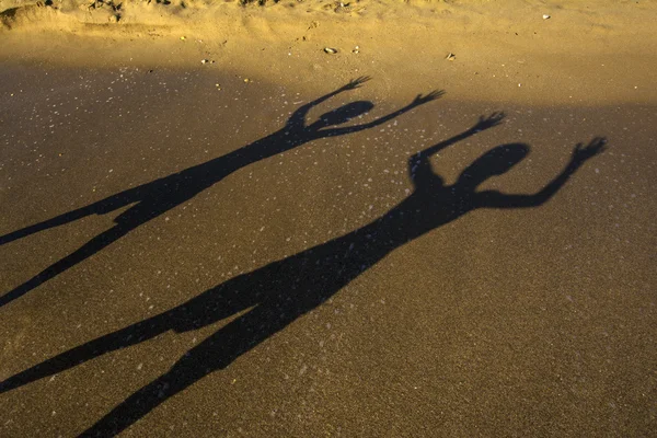 Brothers standing at water s edge on beach casting shadows on sand in Corfu, Greece