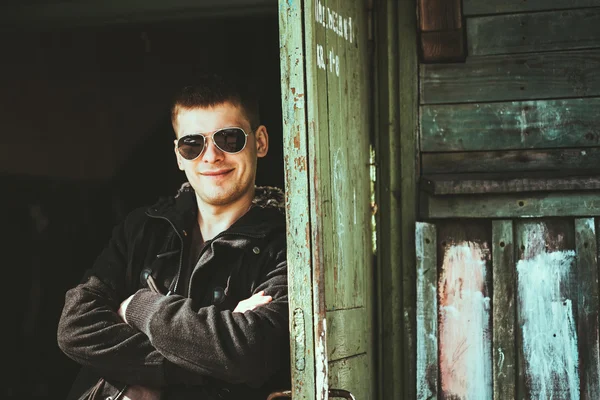 Young handsome man staying near old wooden house in autumn or sp