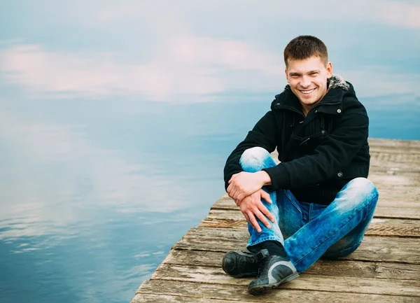 Young handsome man sitting on wooden pier, relaxing,  thinking.