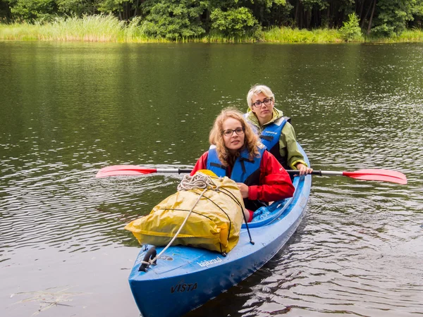 Two young girls wearing life-jackets and sitting in a kayak.