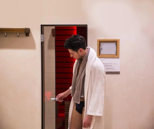 Young man in bathrobe entering or exiting sauna