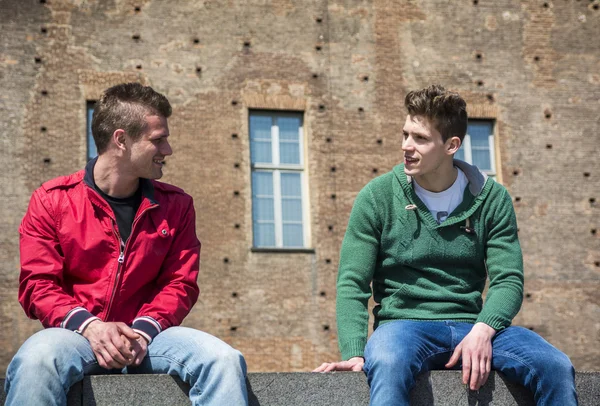 Two young men talking while sitting on curb