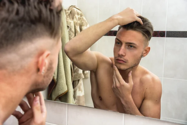 Young man touching his face while looking in mirror