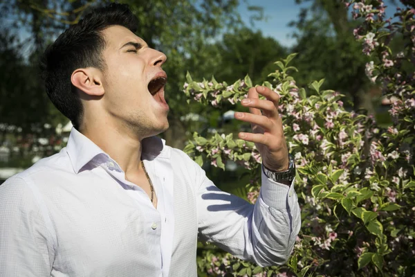 Young man next to flowers sneezing
