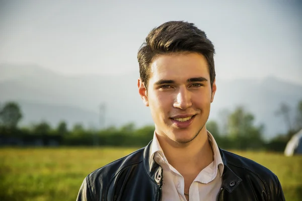 Handsome smiling young man at countryside, in front of field or grassland