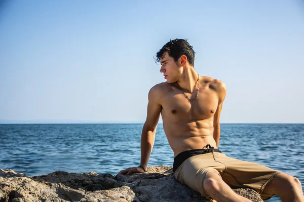 Young shirtless athletic man crouching in water by ocean shore