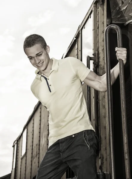 Fit guy with polo shirt hanging from old train, jumping