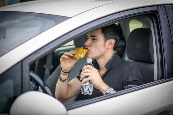 Young man driving his car while eating food