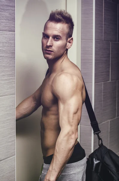 Shirtless muscular young man opening door, with gym bag