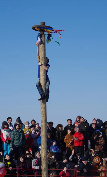 Shrovetide in Russia. Man climbing the pole for prize during win