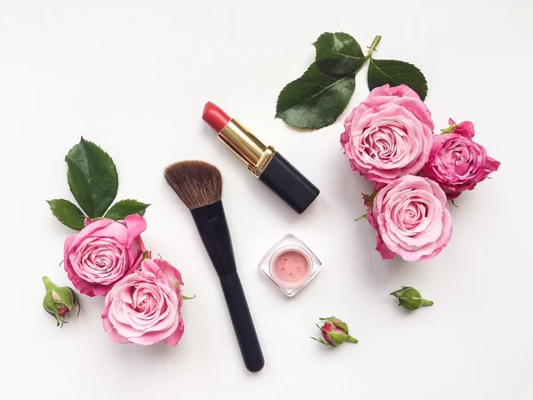 Decorative flat lay composition with cosmetics and flowers. Top view on white background