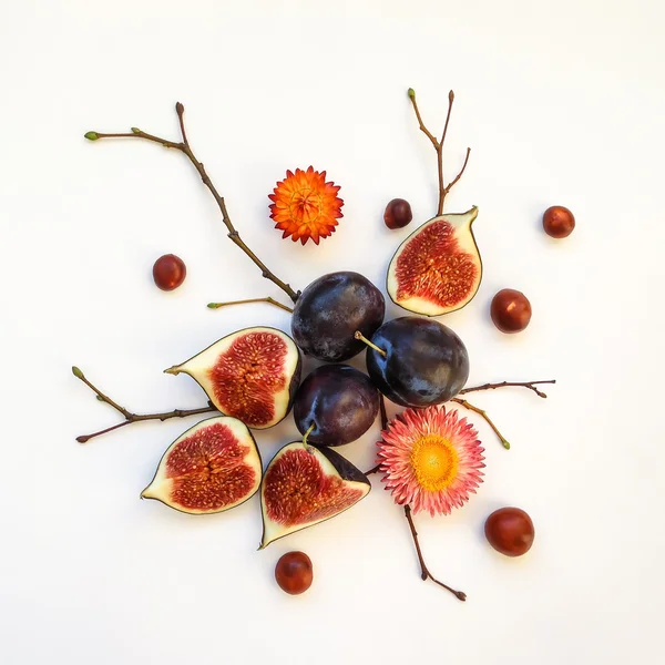 Bright autumn composition of plums, figs, dry flowers and branches on white background. Flat lay, top view