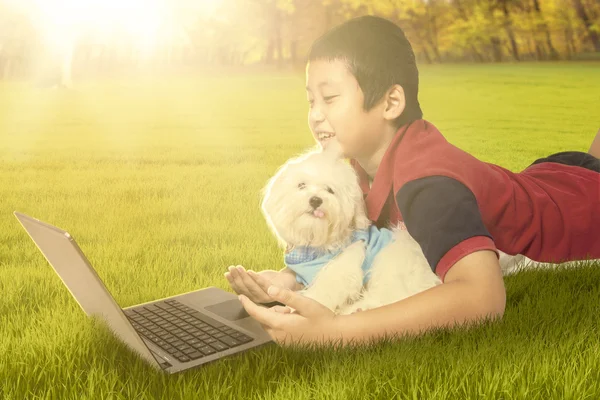 Cute boy using laptop with his puppy at the park