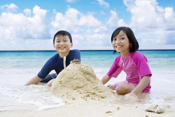 Cheerful children and sandcastle at beach