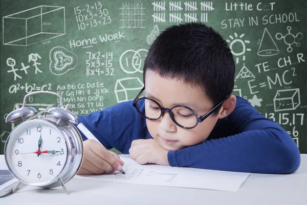 Adorable boy studying with alarm clock