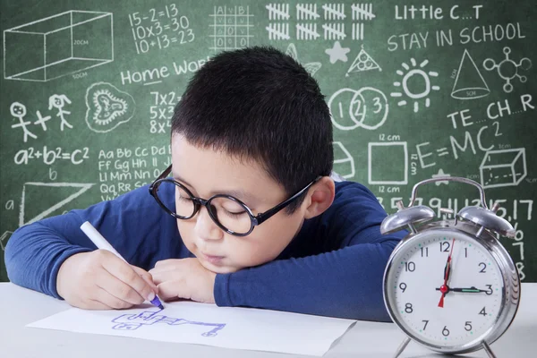 Schoolboy studying with a clock on the table