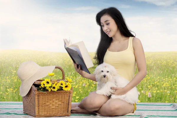 Cute woman and dog read book at field