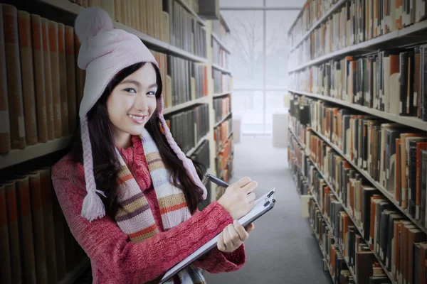 Student with sweater and clipboard in library