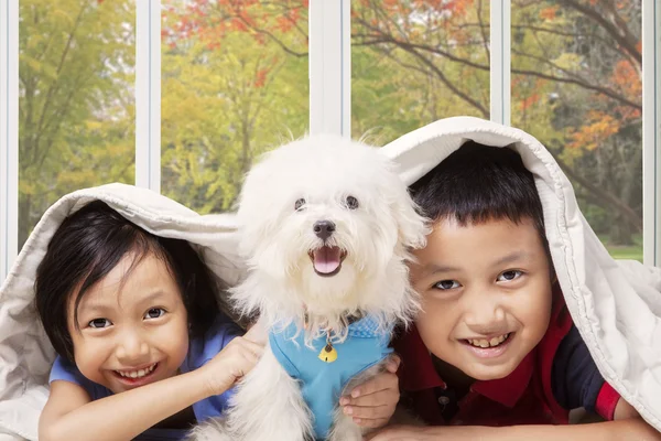 Two children lying under blanket with dog